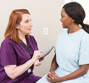 Healthcare provider with digital tablet talking to woman in exam room.